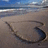 Pixelated beach scene with blue sky, ocean waves, and a dark curved shape on sandy shore.