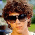 A person with curly brown hair and dark sunglasses appears in a of four , each showing slightly different head angles against an outdoor background