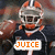 Pixelated image of a football player in a dark uniform with orange accents, wearing a helmet, holding a sign with text.