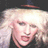 Pixelated close-up of a person with light-colored hair and dark clothing against a dark background.