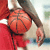 Pixelated static image of a basketball player in red uniform holding an orange basketball, with visible arm and torso details against a light background.