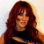 A woman with long red hair in a black top with horizontal stripes, smiling against a light background with a colorful abstract lower section.