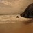A pixelated static image shows a small dark shape on light brown ground near a large dark mass against a gradient sky.