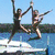 Two people jump from a white boat into blue water, one person performs a handstand on a wooden floor indoors, three people pose outdoors with greenery.