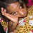 Pixelated image of a person with light brown skin wearing a yellow patterned top, holding their hand near their face in a gesture.