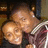 Pixelated image of two figures in close embrace, one with light skin and short hair, the other with darker skin and long hair, both wearing dark clothing.