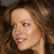Pixelated close-up of a person with light skin tone, brown curly hair, and red lips, showing a slight smile.