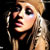 Pixelated close-up of a person with long blonde hair and dark eye makeup against a black background, rendered in low-resolution 50x50 pixels.