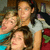 Four people in a group pose with varied clothing colors including teal, white, and red, against a blurred background.