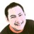 Pixelated static image of a person with short dark hair, closed eyes, and a slight smile wearing a dark top with an orange collar.