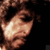 A pixelated close-up of a person's face with dark hair, showing a bright reflection on the cheek against a dark background.