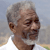 Pixelated close-up of a person with short gray hair, light skin, and a neutral expression against a blurred background.