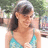A pixelated image of a person with dark hair wearing a light blue bikini top, standing outdoors with green foliage in the background.