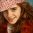 Pixelated image of a person with brown hair wearing a red jacket and pink patterned head covering, set against a bright blue background with red text.