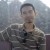 Pixelated static image of a person in a camouflage-patterned shirt against a blurred background.