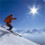 Pixelated static image of a skier in mid-air against a blue sky with sun, on snowy terrain.