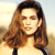 A pixelated close-up of a person with long brown hair wearing a light-colored top against a blurred background.