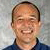 Pixelated portrait of a person with short brown hair wearing a dark blue collared shirt against a light gray background.