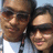 Two people in close proximity, one wearing a white shirt and the other in a dark top, with a light blue sky background.