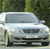 A silver sedan with a dark grille and headlights is positioned in front of a blurred green background of foliage.