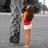 A pixelated image of a woman with long brown hair wearing a red crop top and white shorts, standing against a gray background with dark shapes.
