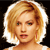 Pixelated close-up of a person with short blonde hair, light skin, and a neutral expression against a black background.