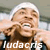 Static buddy icon featuring a pixelated close-up of a person with light brown hair wearing a white headband and dark clothing, with the name "ludacris" in large white text at the bottom.