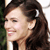 A pixelated close-up of a person with dark brown hair, a white hair clip, and a light-colored top, smiling with eyes closed against a blurred background.