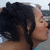 Pixelated profile view of a person with dark curly hair, light skin, and a neutral expression against a blurred background.