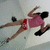 A person in a pink top and red shorts lies on their back with legs extended, arms raised above the head, wearing black shoes.