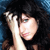 Pixelated image of a person with dark hair holding a light-colored object near their face against a blue and black background.