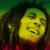 Pixelated static image of a person with yellow-toned skin, dark hair, and green background elements.