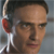 Pixelated close-up of a person's face with short dark hair, visible ear, and partial neck, set against a blurred background.