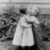 Black-and-white animation of a figure in long dress standing outdoors with arms extended, background foliage visible.