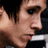 Pixelated close-up of a person's face with light skin tone, dark hair, and visible eye details against a dark background.