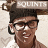 Pixelated image of a person wearing dark hair, glasses, and a black earpiece with visible text above the head.