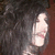Pixelated static image of a light-skinned figure in a white dress with pink accents against a dark, indistinct background.