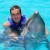 Pixelated image of a person in a blue top holding a dolphin against a light blue background.