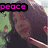 A pixelated image of a person with long dark hair holding an object near their face, set against a green background with pink text reading 'peace' in the top-left corner.
