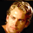 Pixelated close-up of a person's face with light brown hair and warm skin tones against a black background, rendered in low-resolution 256x256 pixels.