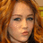 Pixelated close-up of a person with curly reddish-brown hair, light skin tone, and visible freckles on the face.
