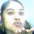Pixelated close-up of a person with long hair wearing headphones, holding an object near their face against a light blue background.