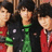Three individuals with dark hair stand side-by-side against a blurred background, wearing red and black clothing with green accents.