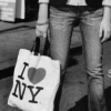 Black-and-white photo of a person holding an 'I ❤️ NY' tote bag, wearing jeans and a short-sleeve shirt.