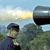 Pixelated image of a person in dark clothing holding a large black and gray object against a sky and tree background.
