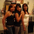 Three women pose together in a dimly lit indoor setting with one woman holding a microphone.