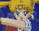 Animated sequence of a blonde anime character in sailor uniform performing actions against blue and green backgrounds with yellow ribbons.