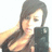 Pixelated image of a person with long dark hair holding a dark rectangular object near their face, wearing a dark sleeveless top against a white background.