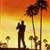 Pixelated static image of two silhouetted figures embracing against a sunset sky with palm trees, rendered in warm orange and yellow tones on a 50x50 pixel grid.