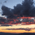 Pixelated landscape showing dark clouds over a horizon with orange and yellow light bands, blue sky above, and dark water below.